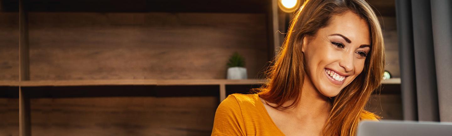 Woman in yellow shirt smiling at her laptop