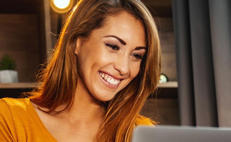 Woman in yellow shirt smiling at her laptop