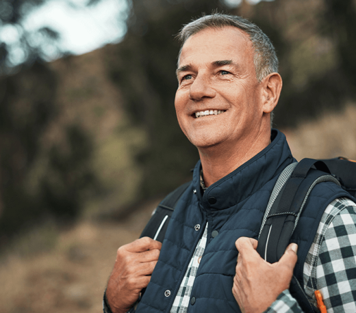 Older man with backpack on outside, smiling